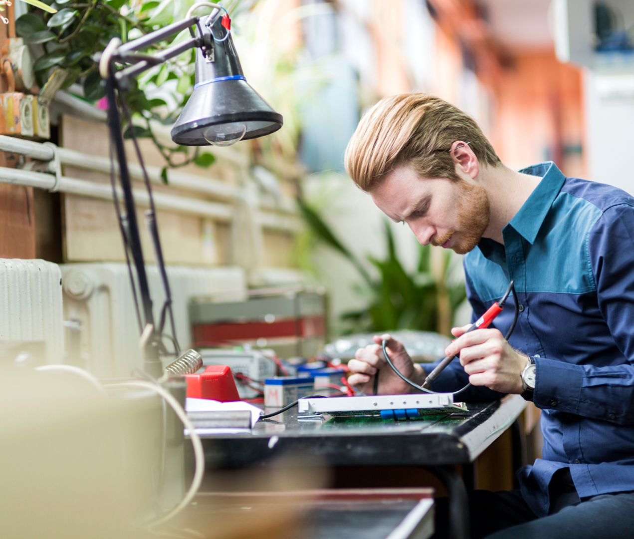 Frame 1618874152 Person soldering components at a workbench.